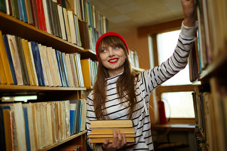 年轻女学生在图书馆架之间选图片