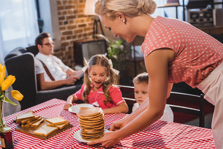 快乐的孩子们看着微笑的母亲把煎饼放在背景图片