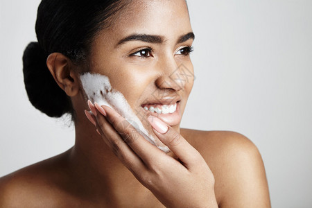 用泡沫在脸颊上清洁皮肤的女人图片