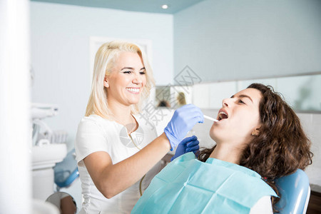 快乐的女牙医在牙科诊所进行检查和清洗病人口腔图片