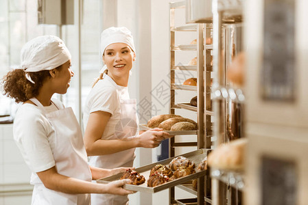 有吸引力的女面包师在烘烤制造时在货架图片