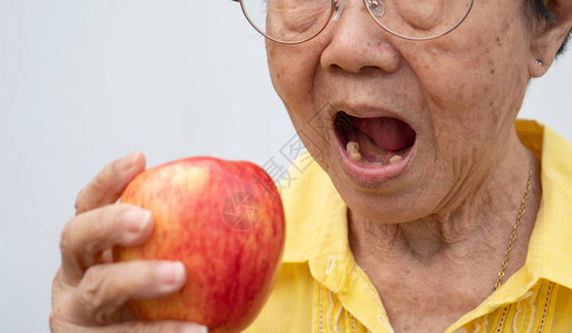 一位戴着眼镜没有牙齿的老妇人试图吃红苹果牙科健康问题概念老年患者背景图片
