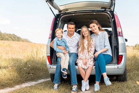 年轻快乐的家庭坐在汽车后备箱里看图片