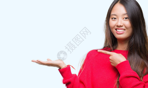 年轻的亚洲女人握着手的东西用手指着她图片