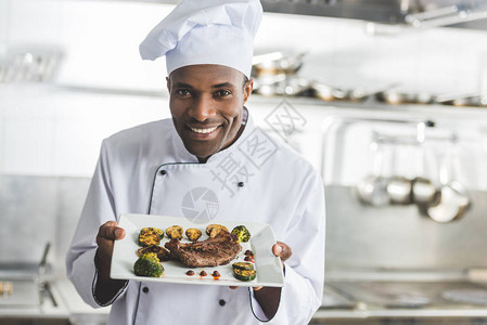 快乐的非洲美食厨师拿着餐盘在餐厅厨房吃图片