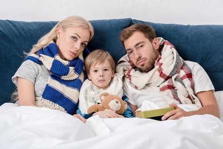 生病的父母和儿子坐在床上看镜头图片