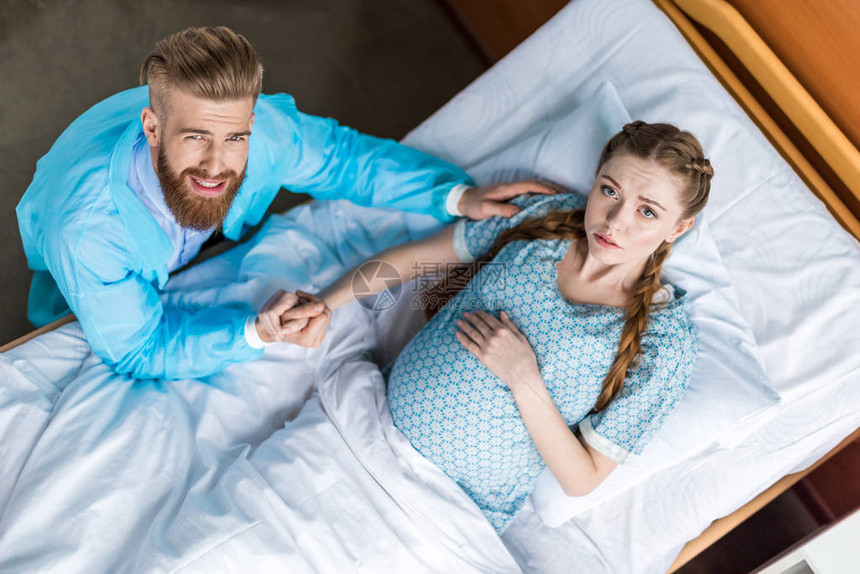 孕妇与丈夫手牵在医院看着相机的俯视图