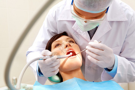 女病人在检查牙齿并钻探牙齿时与牙医图片