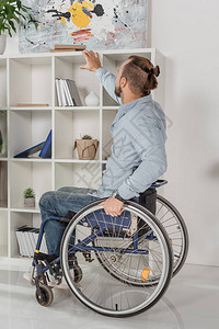 坐在轮椅上的残疾人试图伸手去拿书架上的书图片