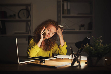 疲倦的女自由职业者晚上在家庭办公室工作图片