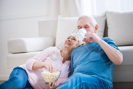 快乐的老年夫妇在家吃爆米花和喝茶背景图片