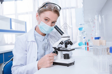 实验室大衣和无菌面具科学家与显微镜合图片