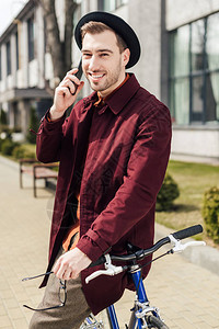 戴眼镜和帽子的时髦男子一边靠着自行车一边靠着图片