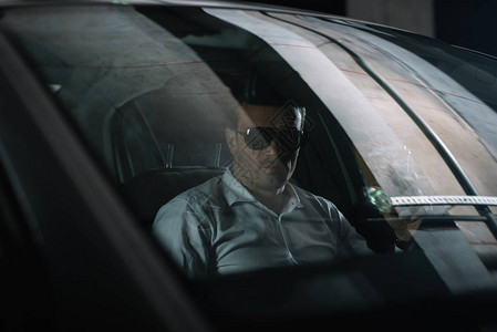 穿着太阳眼镜的男卧底特工在监视时坐在车里拿着纸杯图片