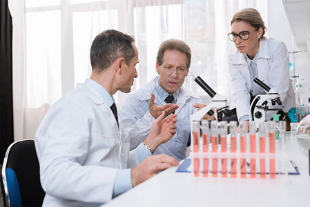 在化学实验室检查和讨论显微镜样本的白大衣医务工作者图片