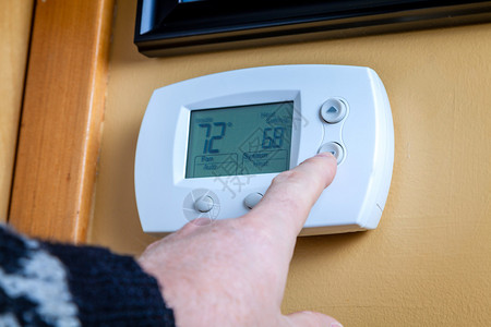 一个人在家庭自动调温器上降低温度Engegr图片
