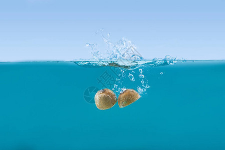 新鲜猕猴桃一半落入水中溅起水花的侧视图图片