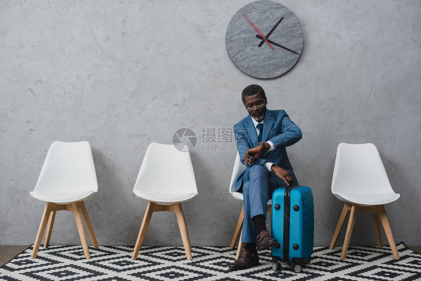 非洲英俊的美籍非洲商人坐在等候室里拿着手提箱看图片