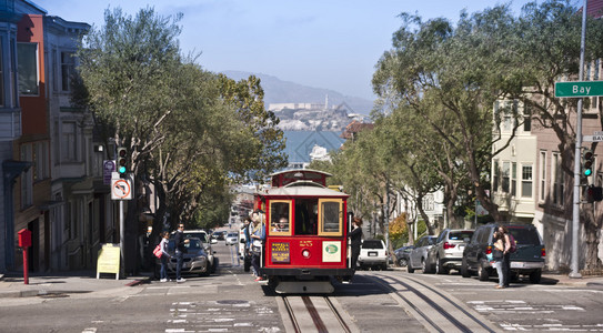 一辆著名的旧金山有线汽车爬上一座山丘俯视着旧金山的阿图片