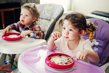 可爱的白种人儿童双胞胎兄弟姐妹坐在高脚椅上吃麦片的肖像图片