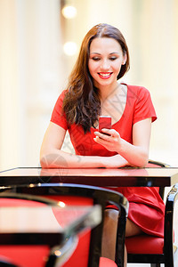 穿着红裙子的美丽笑脸女孩坐在咖啡馆里图片