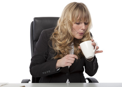 女商人吹着一杯热咖啡当她试图冷却下来这样她可以喝它然后回到工图片