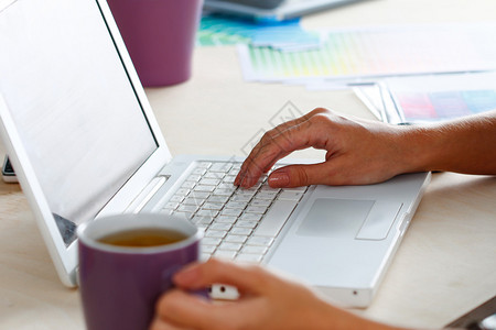 早茶必备女设计师手拿着一杯热饮和使用笔记本电脑喝咖啡早茶的雇员妇女工作日咖啡休息时间创意人士设计图片