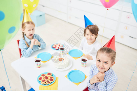 可爱的小女孩和男孩坐在幼儿园的生日桌图片