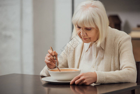 坐在桌边吃奶油汤和在家吃奶油汤的白发长着灰色头图片