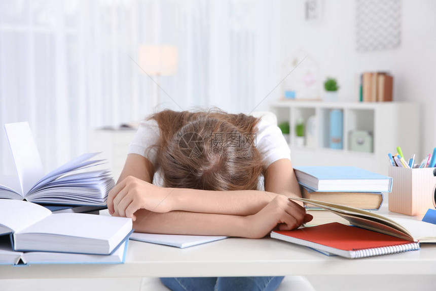 疲倦的学生睡在她的办公桌前准备考试图片