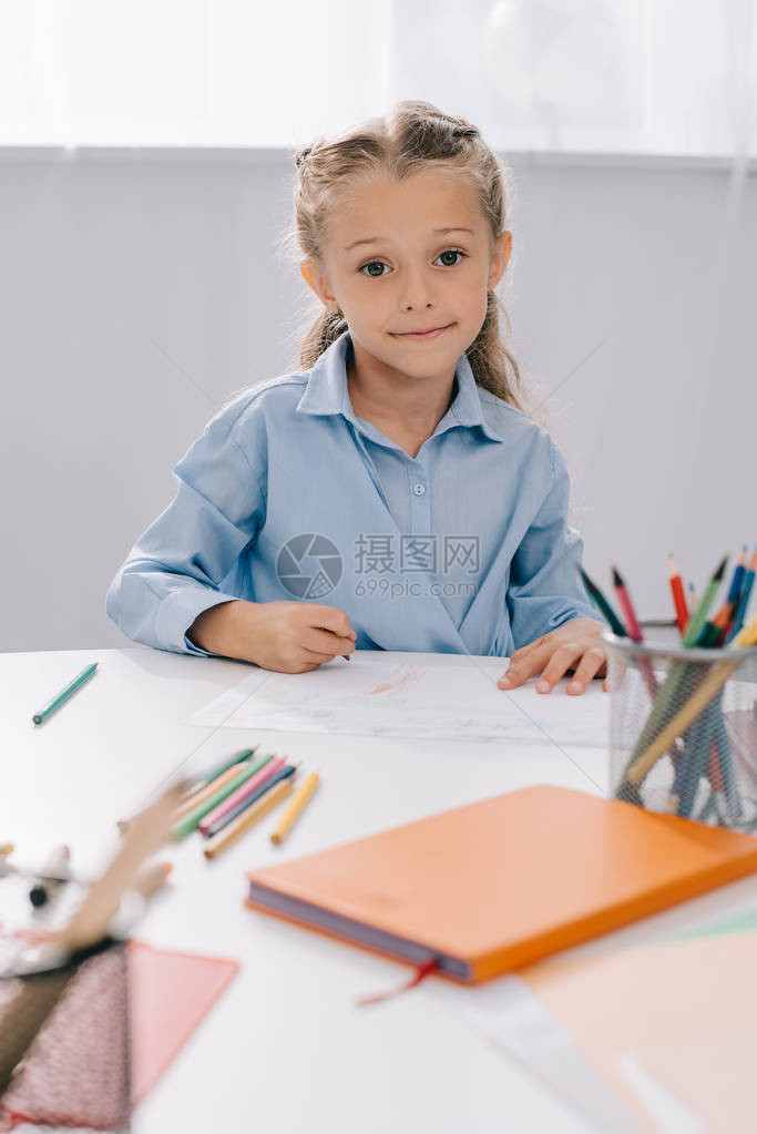 带着彩色铅笔和绘画纸坐在桌边的图片