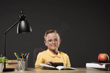 男孩在餐桌上使用带书本植物灯彩铅笔苹果时钟和灰底教科图片