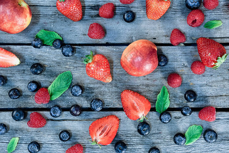 木制桌面上新鲜油桃蓝莓草莓和薄荷叶的顶视图图片