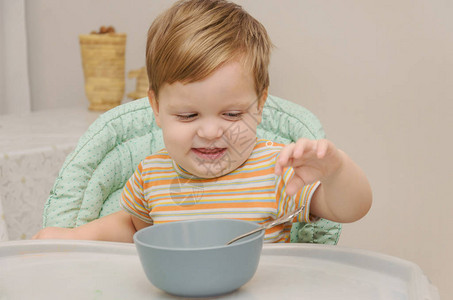 穿条纹T恤衫的金发小金发男孩用灰色盘子上的勺子吃粥图片