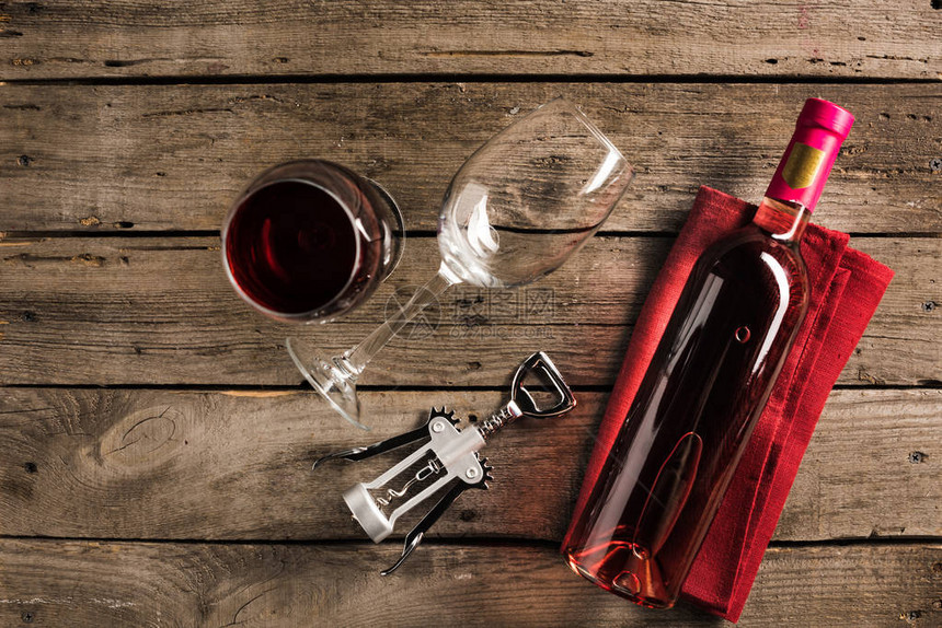 红色餐巾纸上粉红葡萄酒瓶子木桌顶上的corkscrew图片
