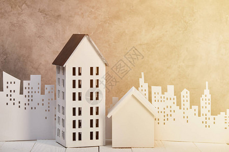 在阳光下的白纸切割城市附近的白色木桌上的房屋模型图片