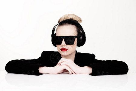 一位戴着墨镜戴着耳机听音乐靠在桌子上看着相机的感女人图片