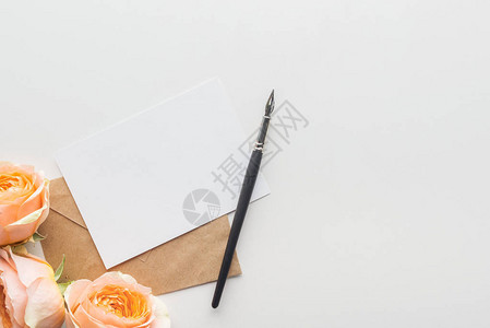 灰色背景上带有棕色信封墨笔和粉红玫瑰的图片