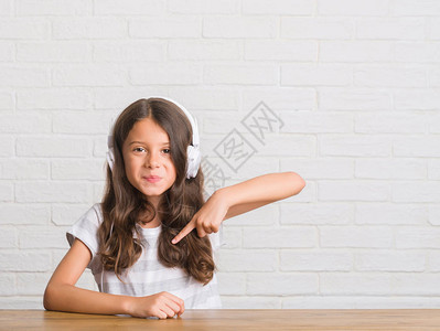 坐在桌子上坐着带耳机的年轻西班牙小孩图片