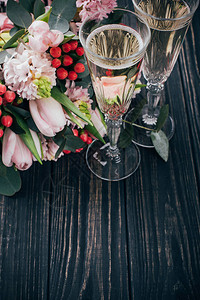 深色木质背景上的两杯香槟和一束粉色鲜花起泡酒和郁金香和风信图片
