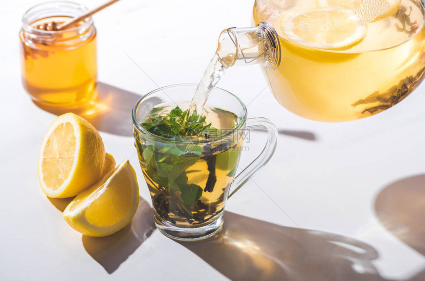用茶壶中的柠檬和薄荷倒上健康的茶水从茶壶到图片