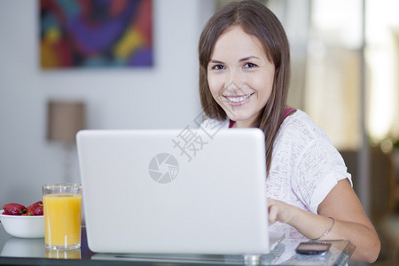 坐在桌子上的妇女用笔记本电脑草莓盘子手机和一杯果图片