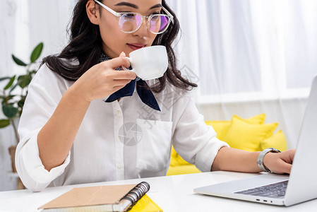 职为有你在家里工作场所使用笔记本电脑和喝咖啡的有吸引力的亚洲自由职背景