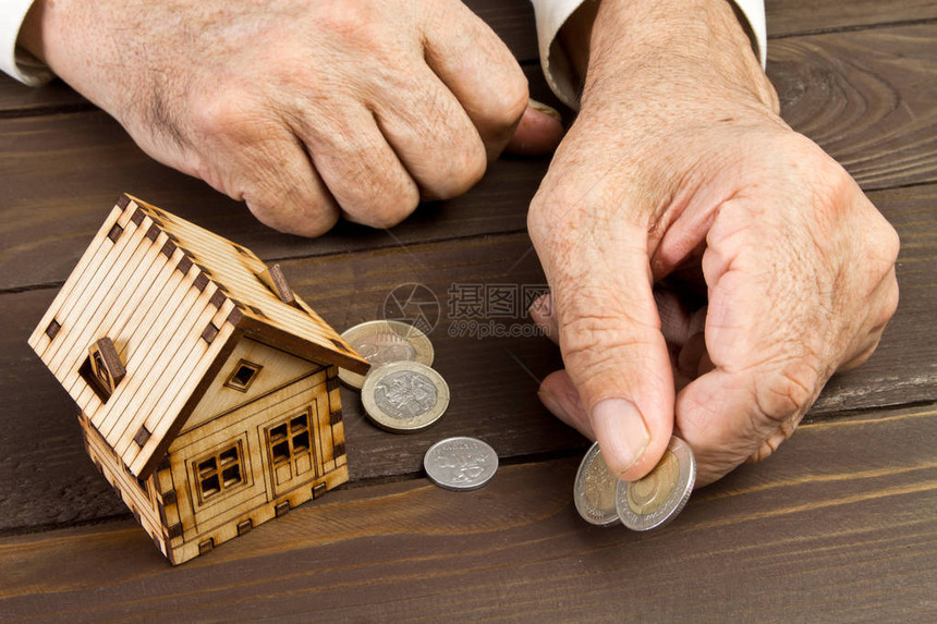 老年人手和有硬币的模范家庭按揭和银行贷款的概念图片