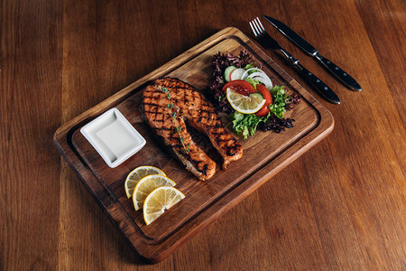 木板上的烤三文鱼牛排配柠檬和生菜图片