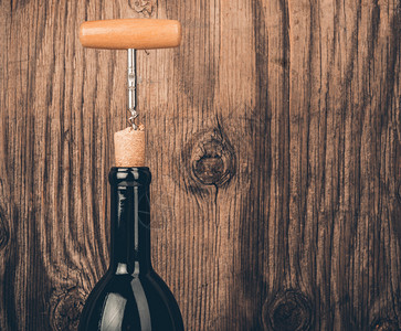 一瓶酒和开瓶器在木制背景图片