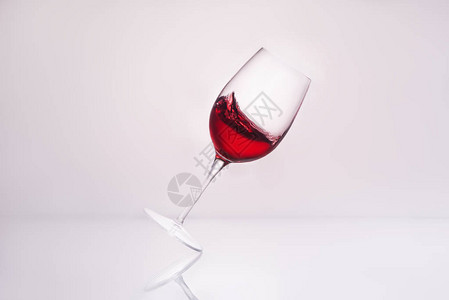 倾斜葡萄酒玻璃在反射表面和背景图片