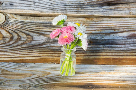 玻璃罐中的鲜花玻璃罐中的雏菊旧松木板的背景图片