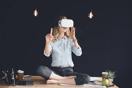 虚拟现实女商人头戴耳机坐在办公室桌上图片
