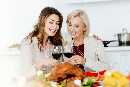 有吸引力的成年妇女与在感恩节宴会桌边的年长母亲喝着葡萄图片